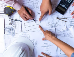 engineers pointing to building on blueprint and using laptop to drawing design building Project in office, construction concept. Engineer concept